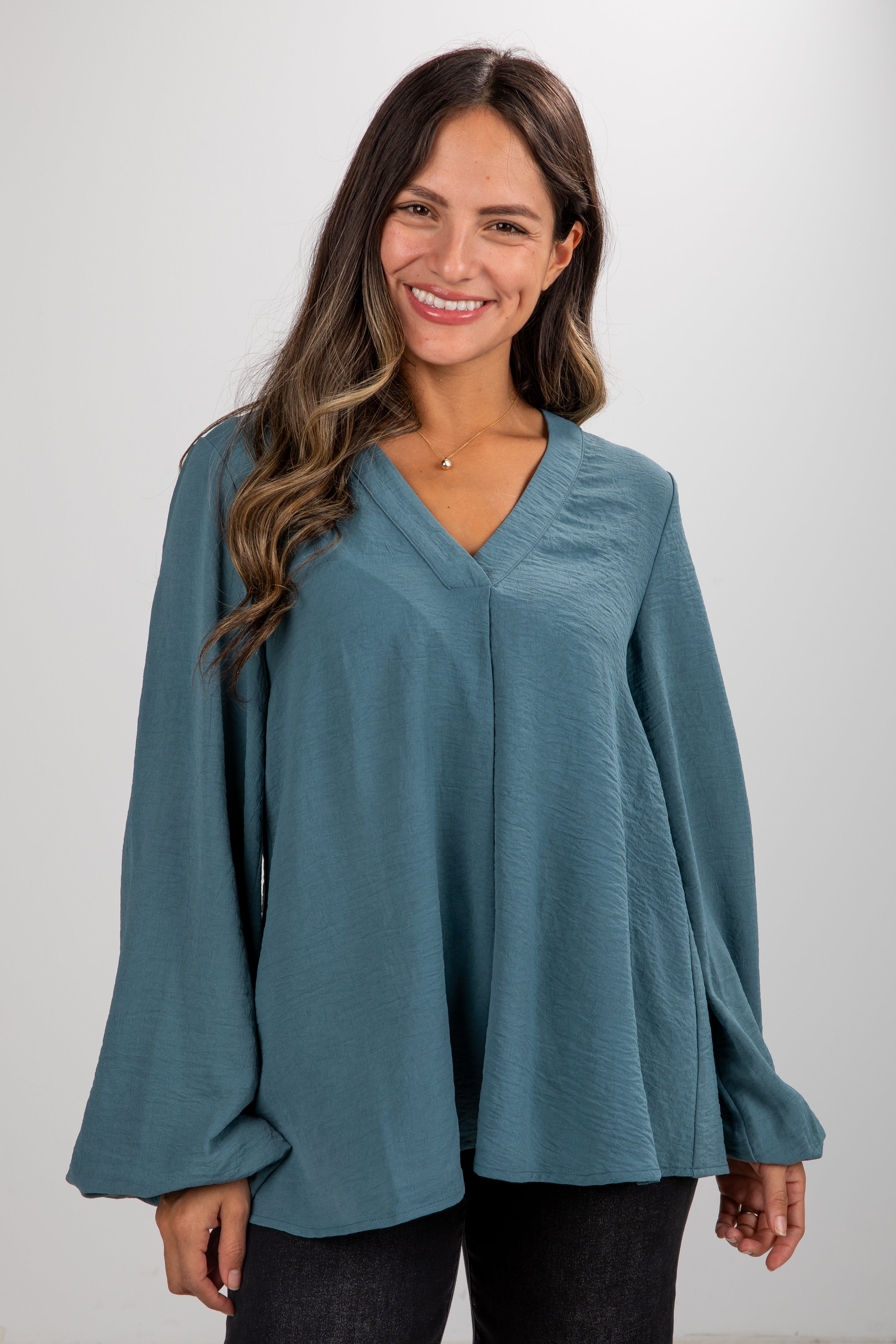 Woman wearing a teal blouse with long sleeves on a white background