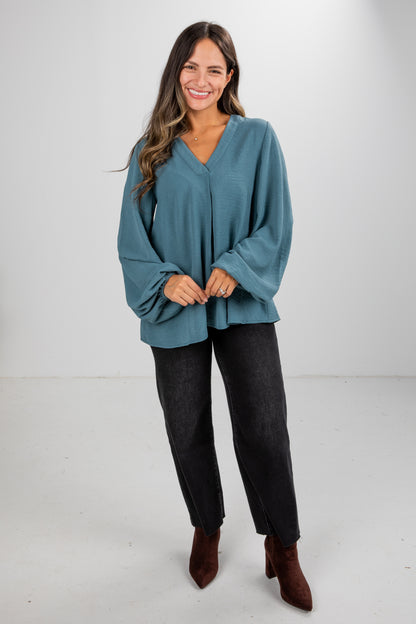 Woman wearing a teal sweater and dark jeans on a white background
