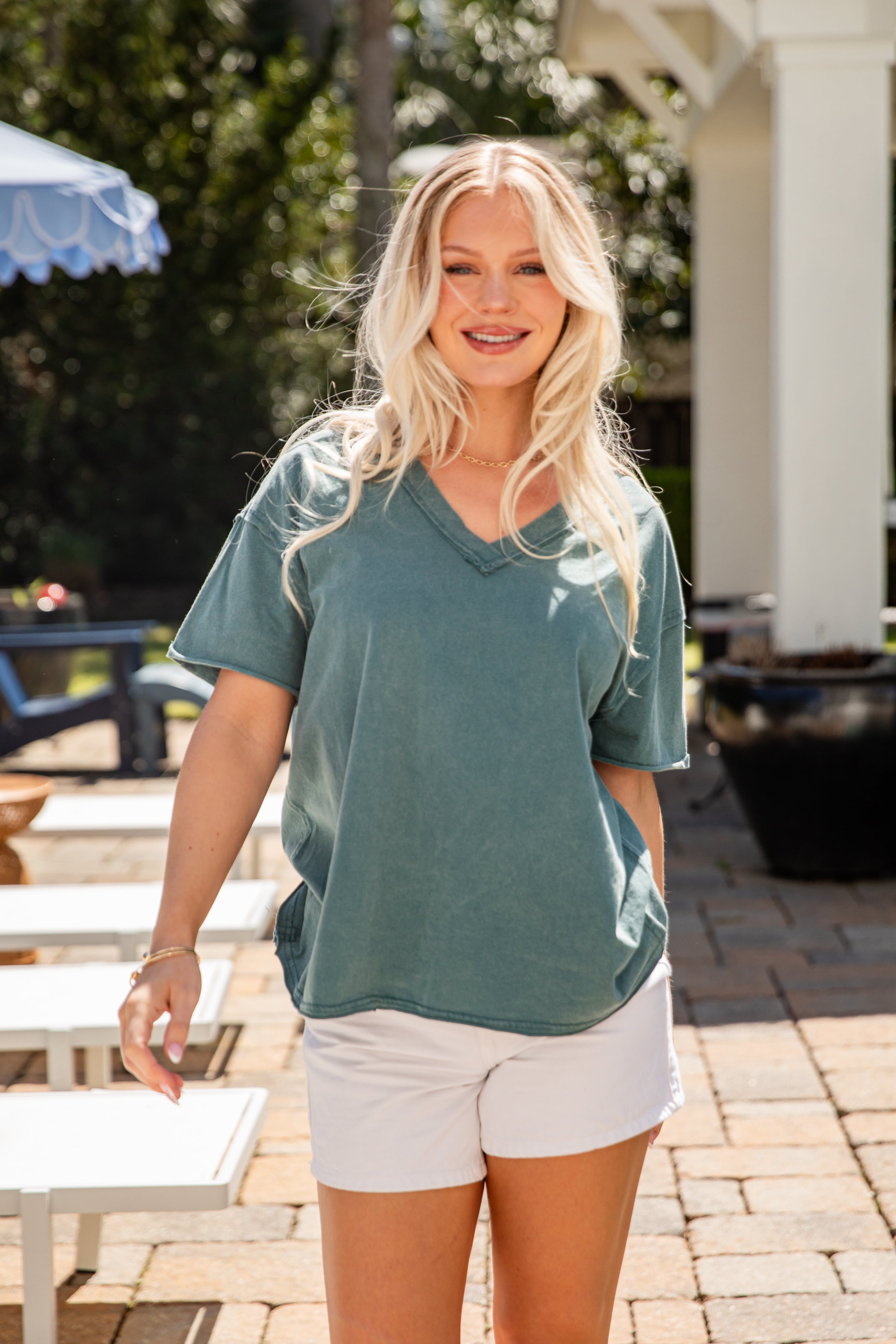 Woman wearing a green shirt and white shorts standing outdoors.
