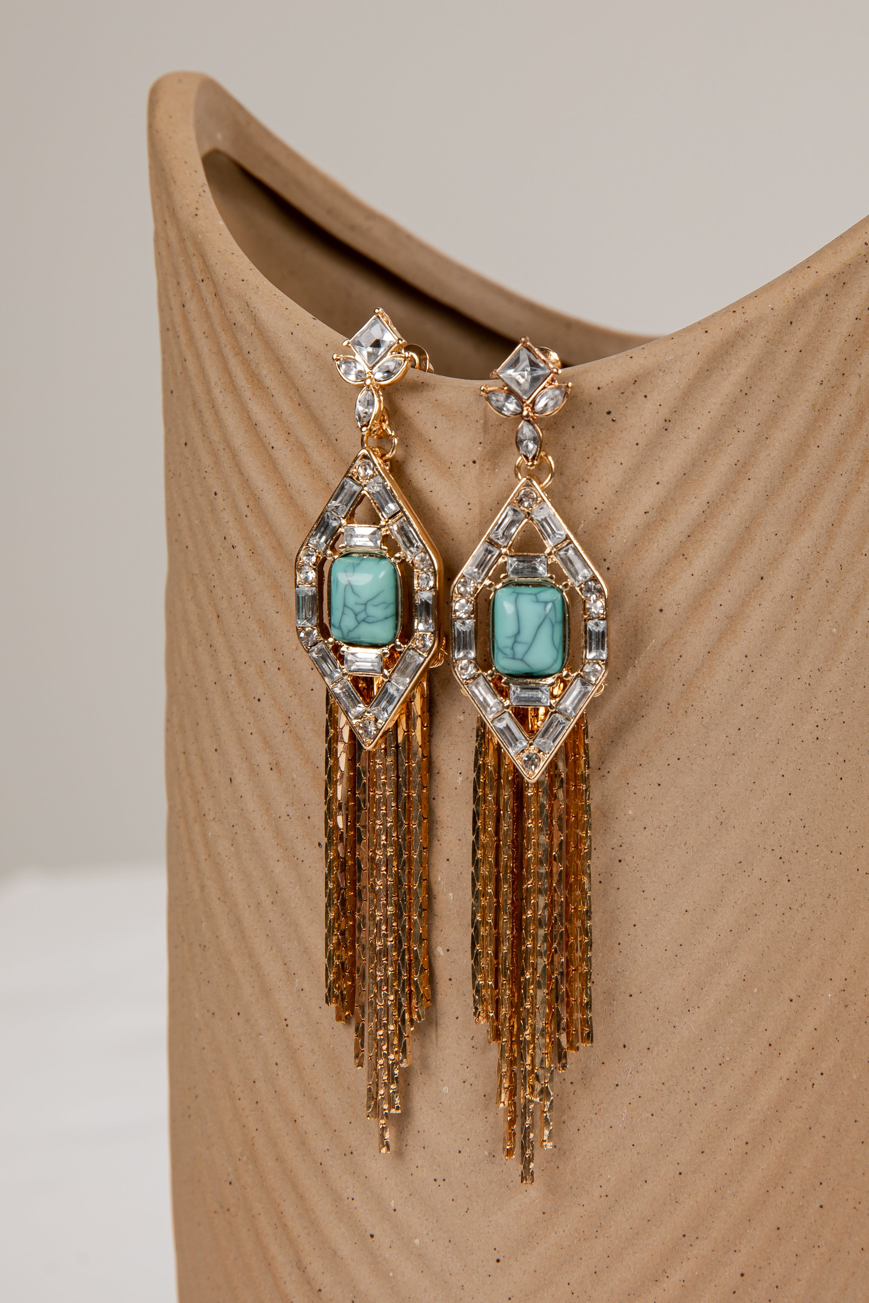 Elegant earrings with turquoise stones and gold fringes on a beige surface