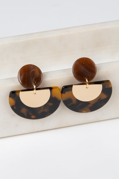 Tortoiseshell and gold half-circle earrings on a marble surface