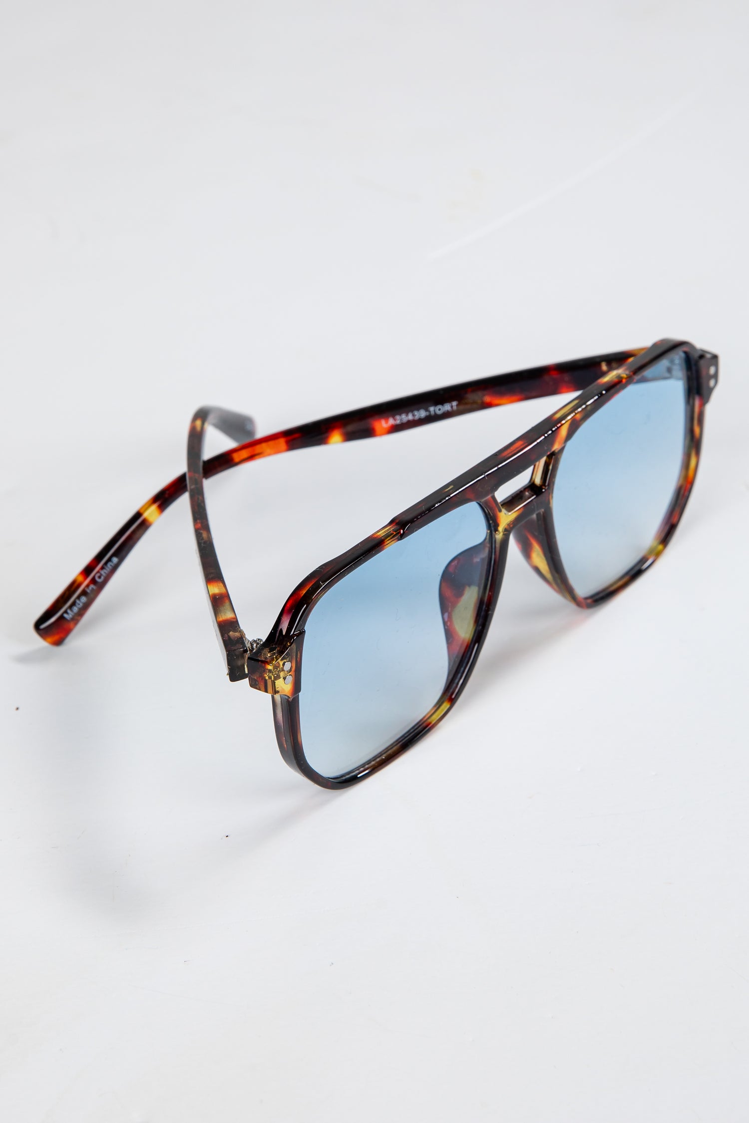 Sunglasses with tortoiseshell frame and blue lenses on a white background