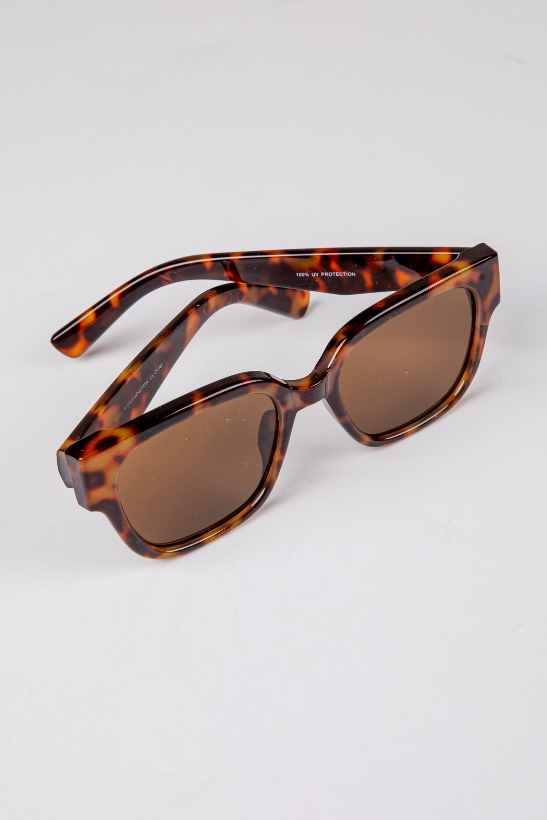 Sunglasses with tortoiseshell frame and brown lenses on a light gray background