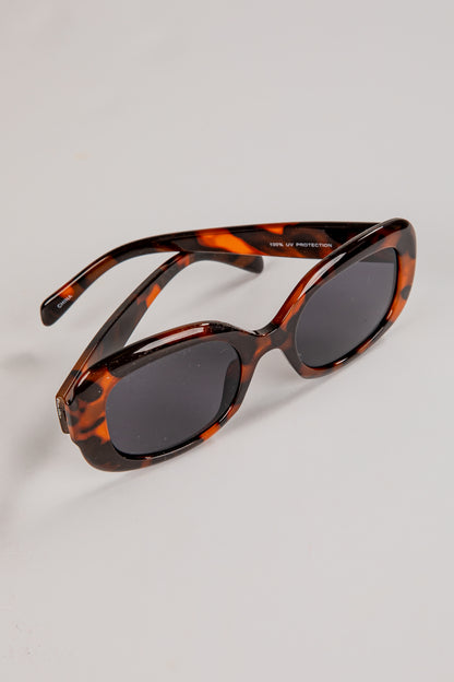 Sunglasses with tortoiseshell frame and dark lenses on a light gray background