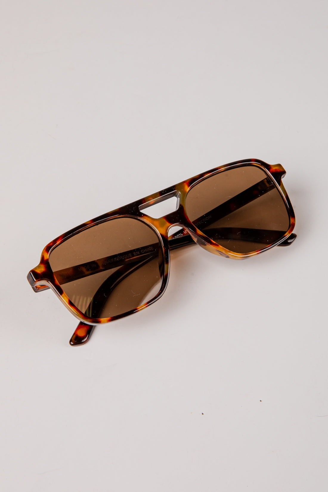 Sunglasses with tortoiseshell frame and brown lenses on a light gray background