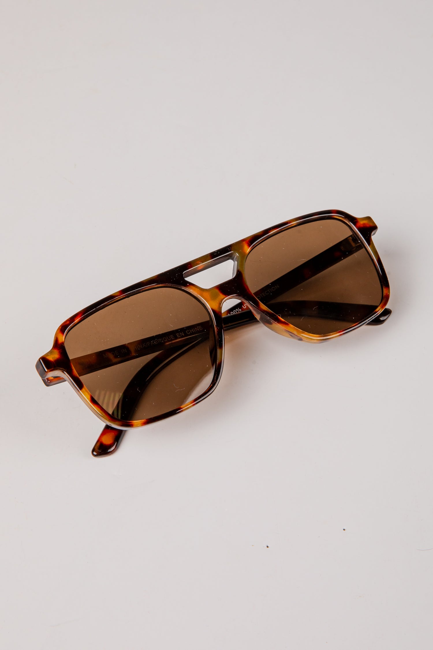 Sunglasses with tortoiseshell frame and brown lenses on a light gray background