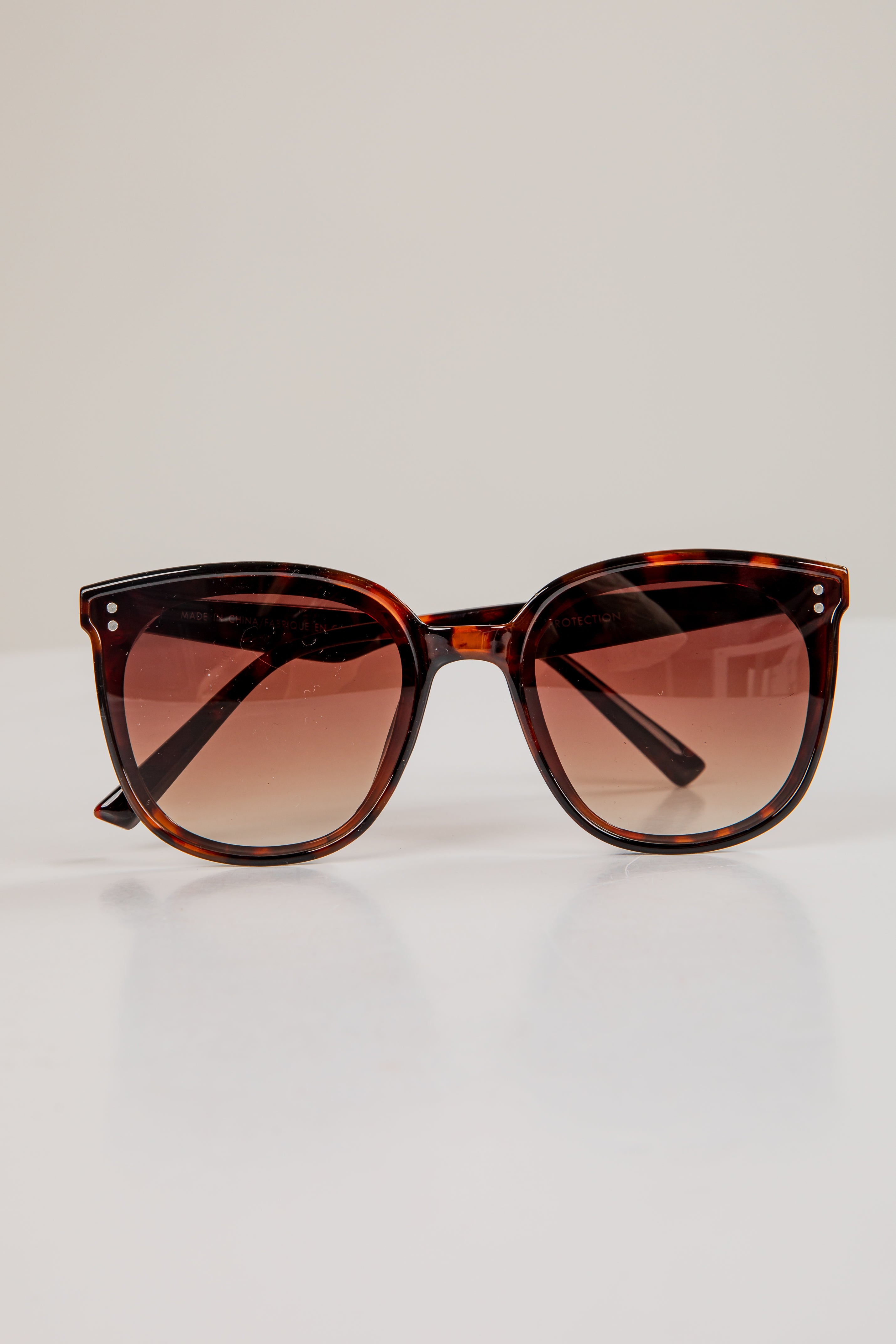 Tortoiseshell sunglasses with brown gradient lenses on a light gray background