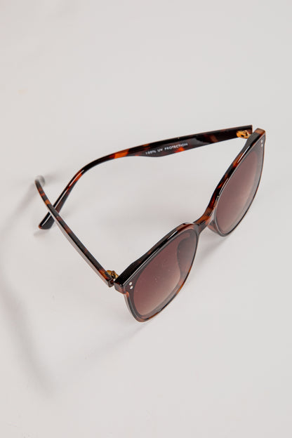 Sunglasses with tortoiseshell frame and brown lenses on a light gray background