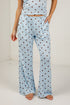 A person wearing light blue pajama pants with dark brown polka dots and a matching top, standing barefoot against a white studio wall.