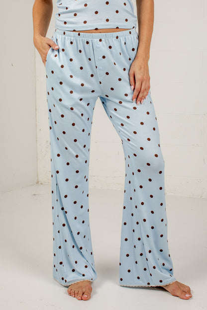 A person wearing light blue flared pajama pants with dark brown polka dots, shown from the waist down against a plain white studio background.