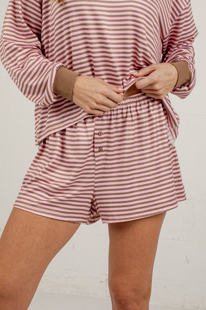 A person wearing a matching striped lounge set with a long-sleeve top and shorts in dusty pink and white horizontal stripes, with brown ribbed cuffs and buttons.