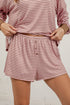 A person wearing a matching two-piece loungewear set with pink and white horizontal stripes, featuring a long-sleeve top and button-front shorts.