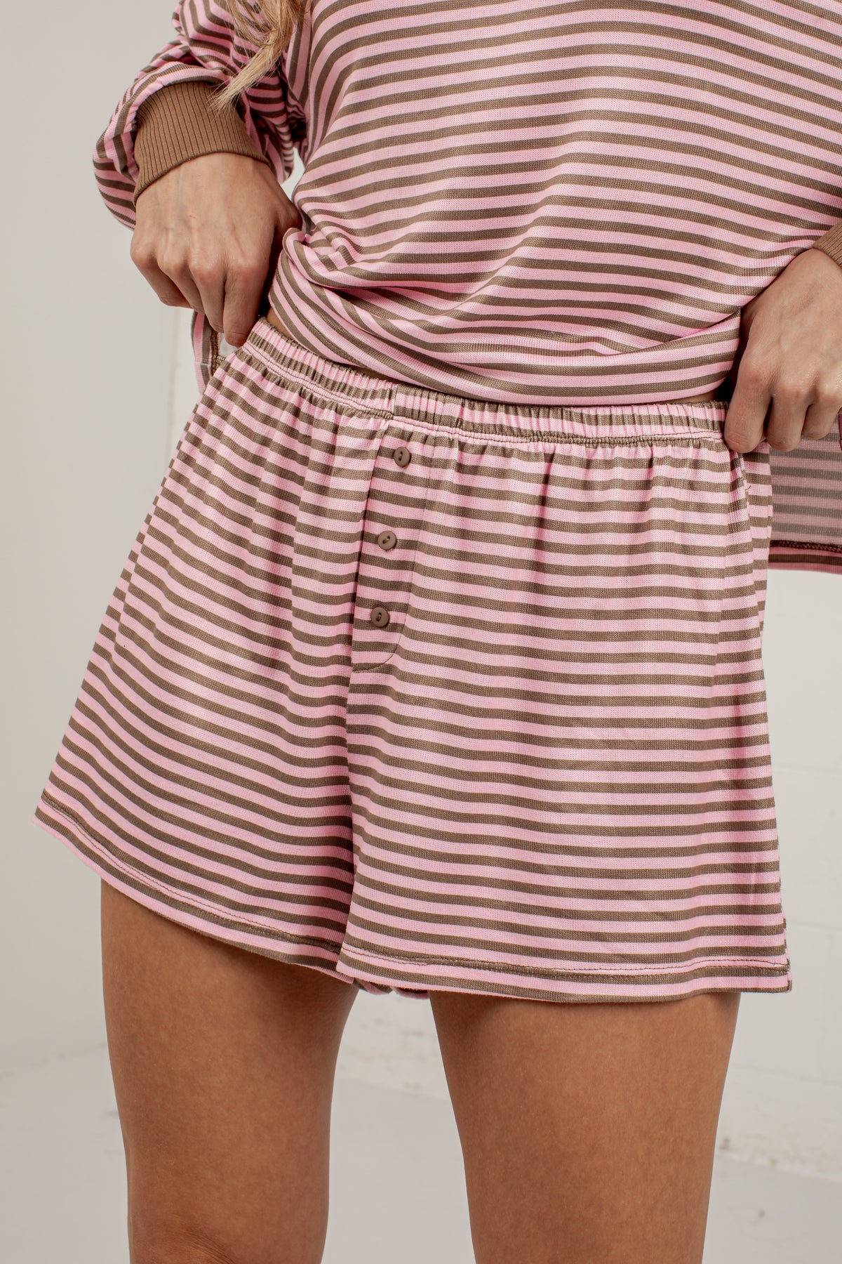 A close-up of a person wearing pink and white striped shorts with a button-front waistband and a matching striped top, photographed against a plain light background.