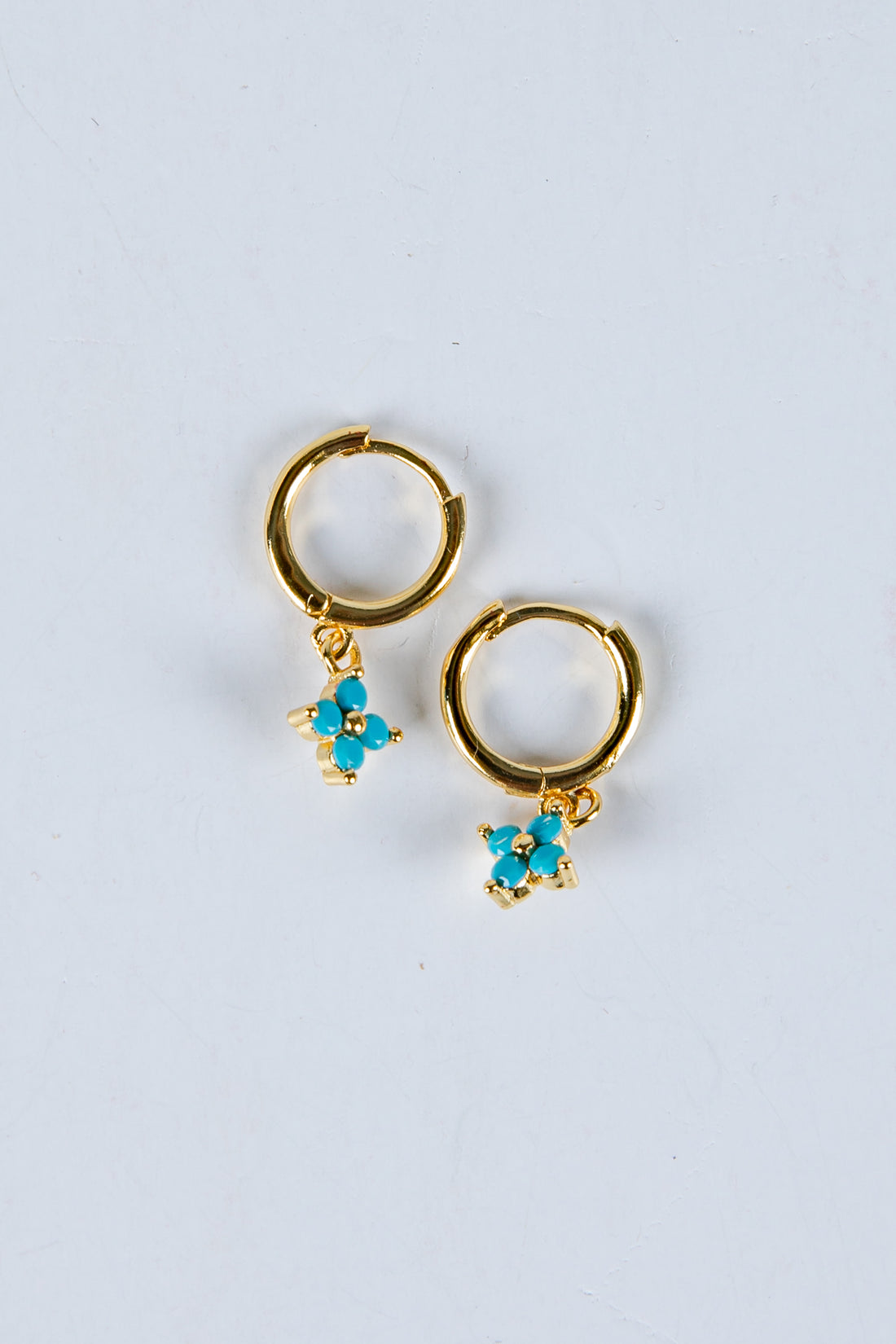 Gold hoop earrings with turquoise flower charms on a light gray background