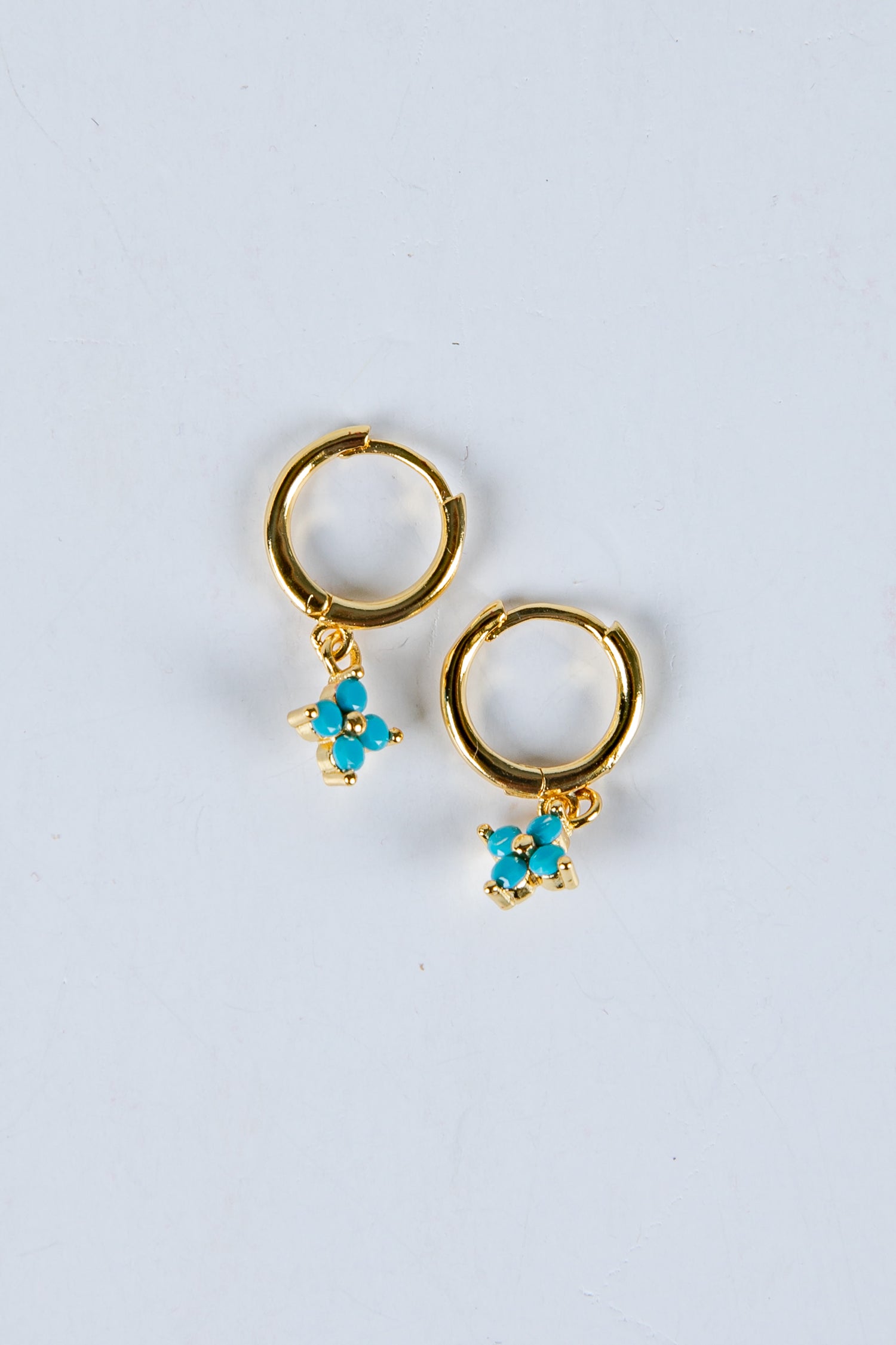 Gold hoop earrings with turquoise flower charms on a light gray background
