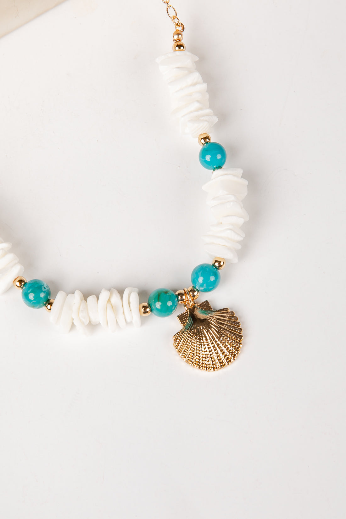 Necklace with white beads, turquoise stones, and a gold shell pendant on a light background