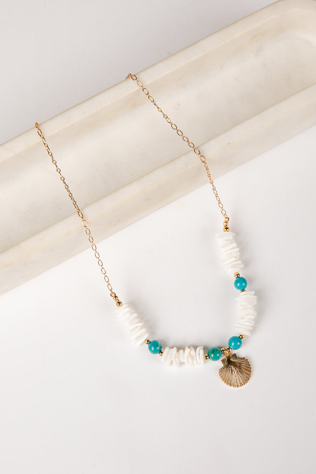 Necklace with white beads and a shell pendant on a light background