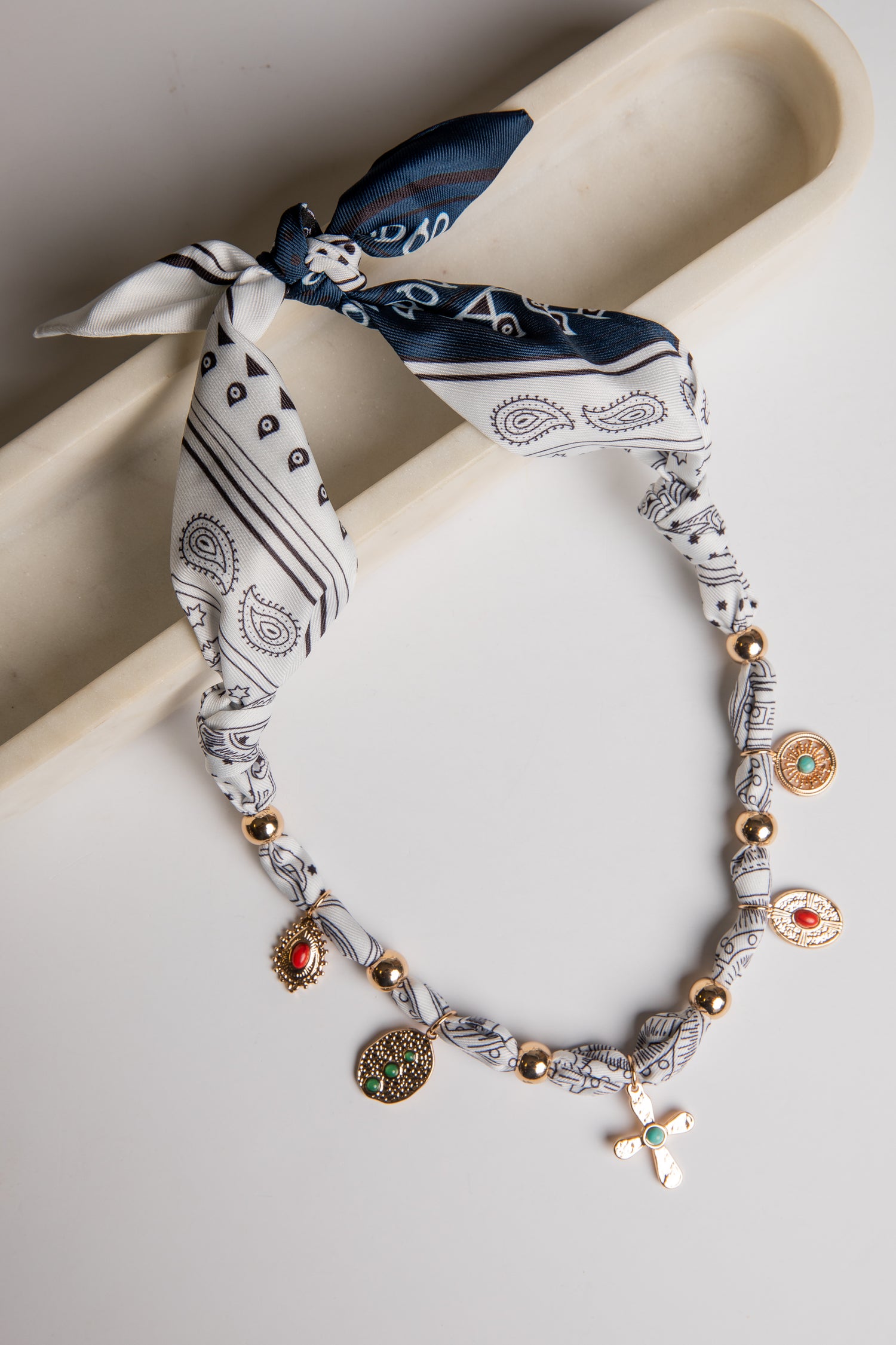 Necklace with charms and bandana-style headband on a white surface