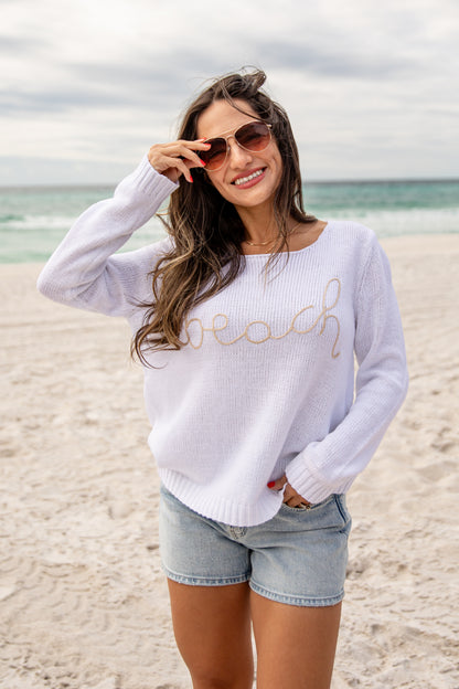 Woman on a beach wearing a white sweater with &