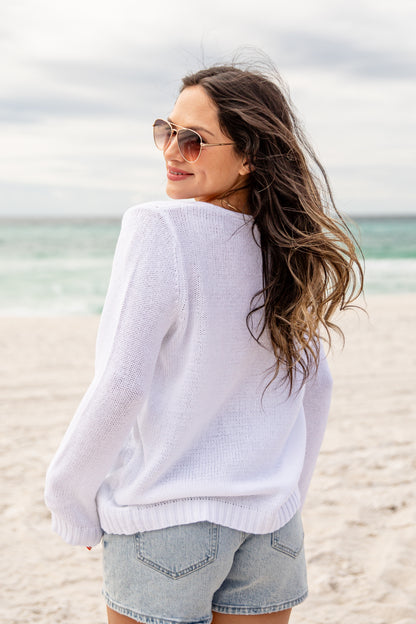 Woman in a white sweater and denim shorts standing on a beach.