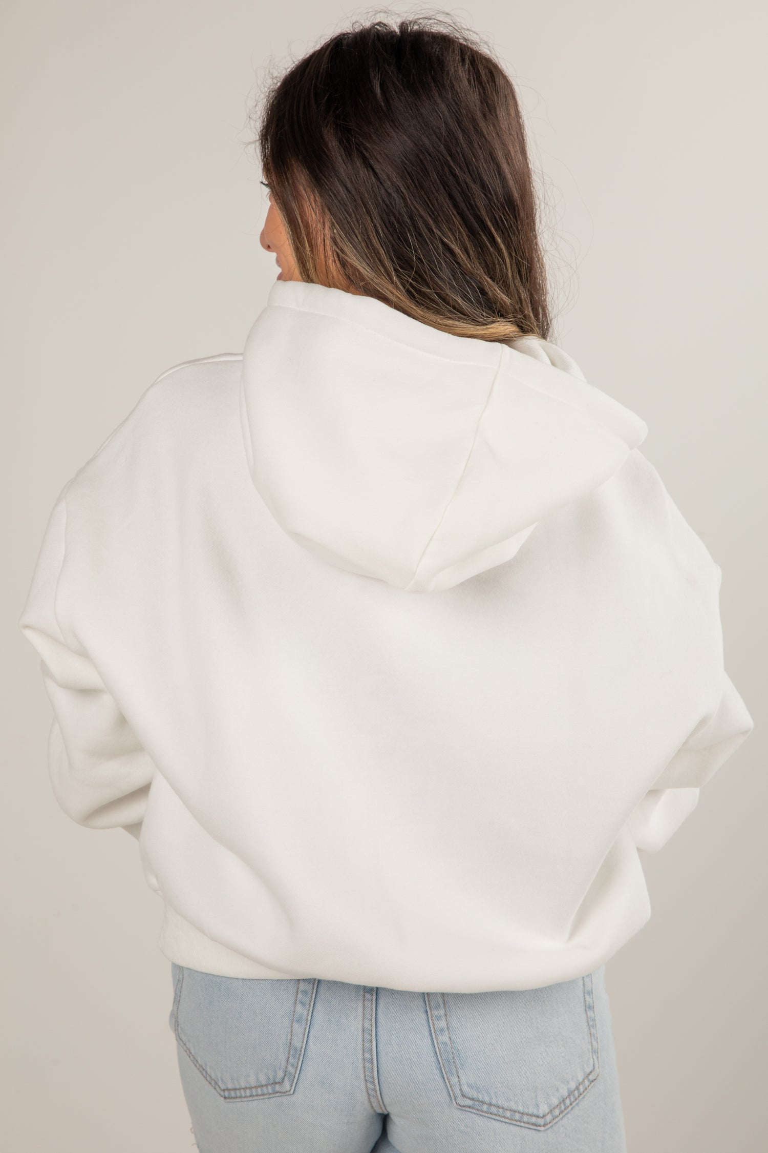 Person wearing a white hoodie and light blue jeans against a plain background