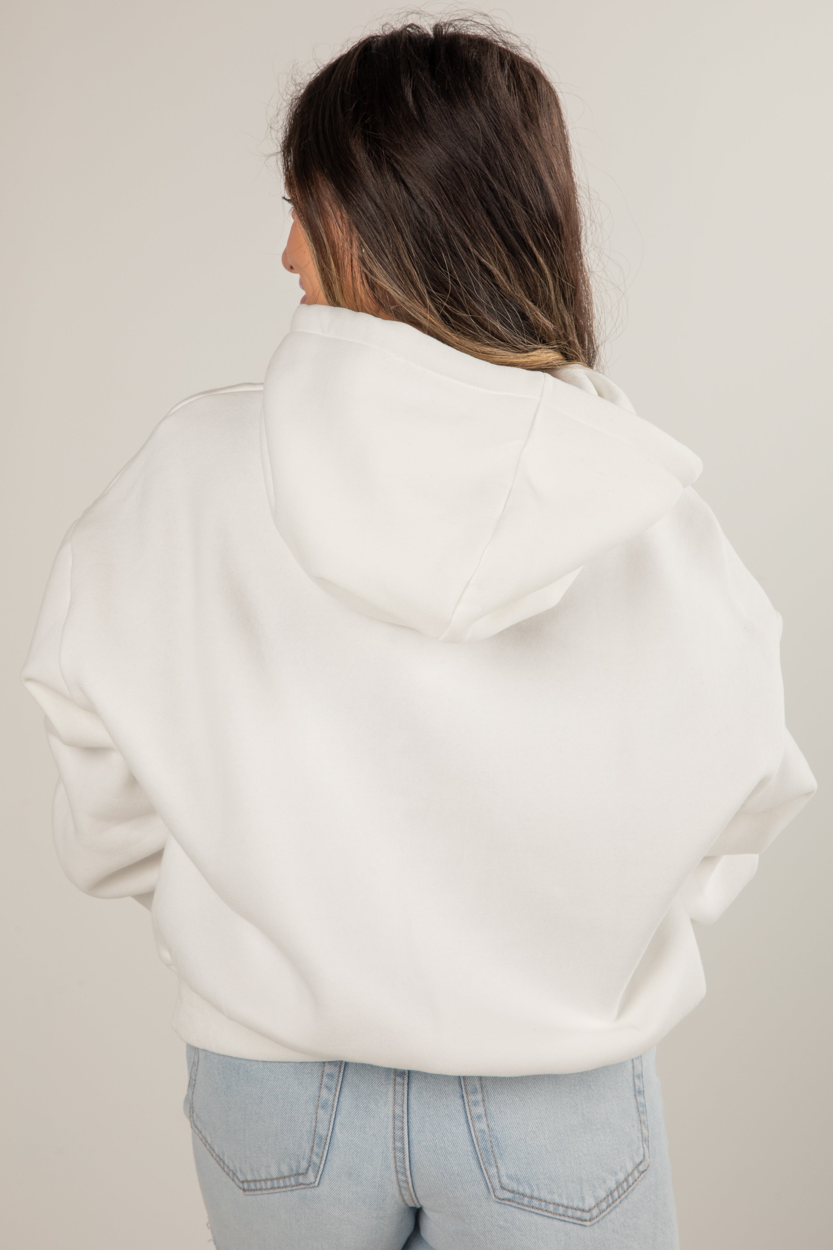 Person wearing a white hoodie and light blue jeans against a plain background