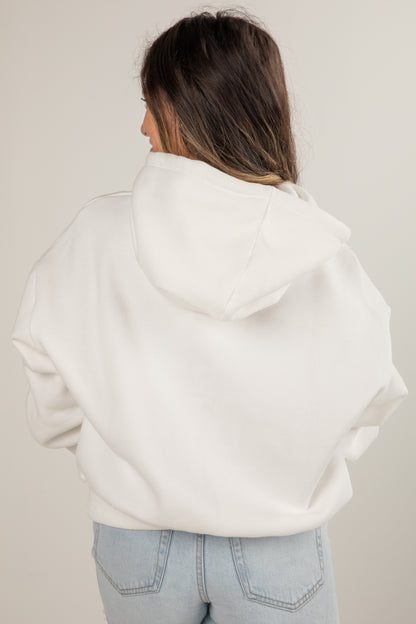 Person wearing a white hoodie and light blue jeans against a plain background