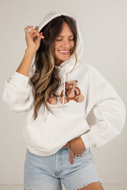 Woman wearing a white hoodie with bear graphics and text, standing against a plain background