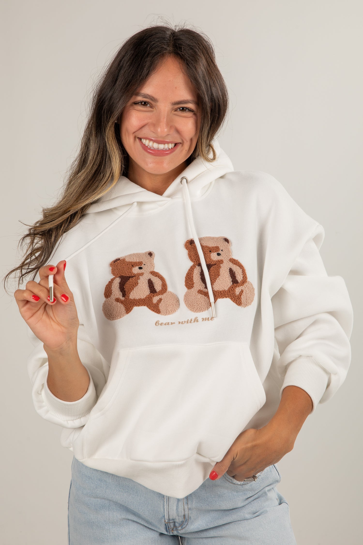 Woman wearing a white hoodie with teddy bear designs and text, holding a small object.