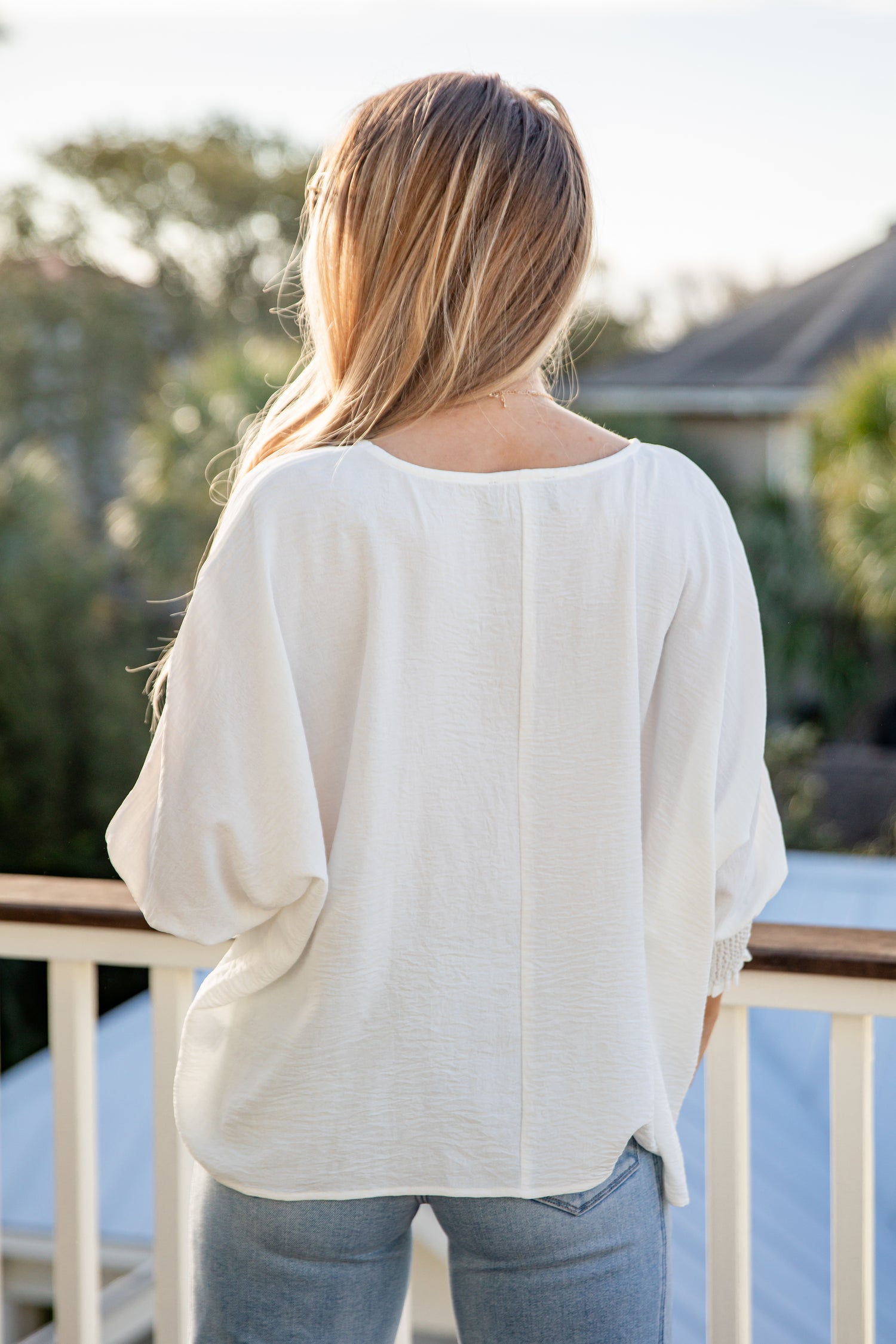 Person wearing a white blouse and jeans standing on a deck with blurred background