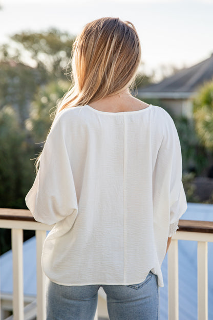 Person wearing a white blouse and jeans standing on a deck with blurred background