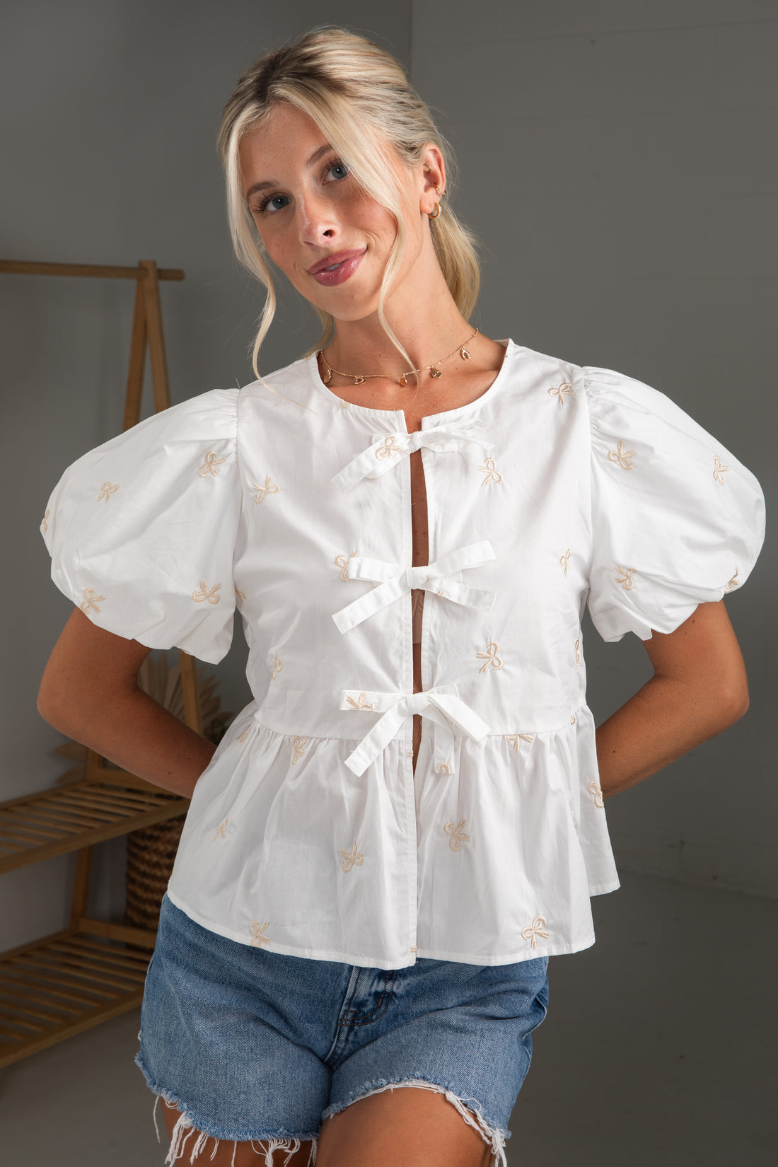 Woman wearing a white blouse with puff sleeves and denim shorts in a neutral setting