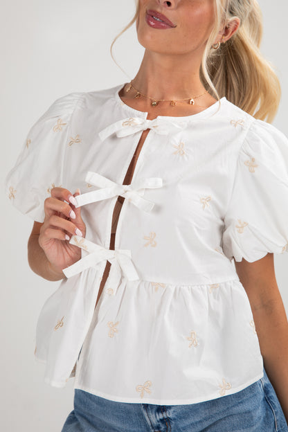 Woman wearing a white blouse with bow details and blue jeans on a plain background
