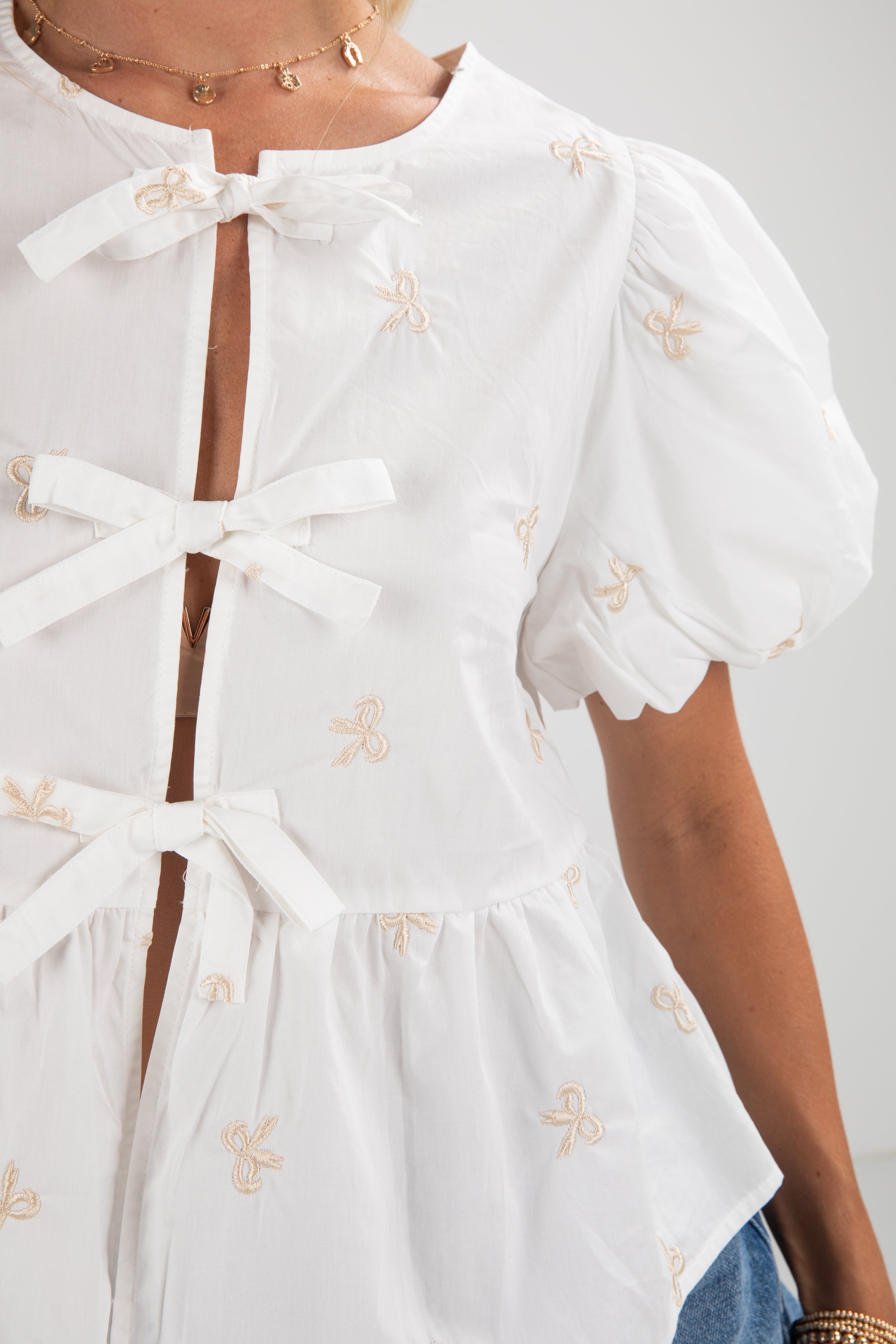 White blouse with puff sleeves and decorative bows on a plain background