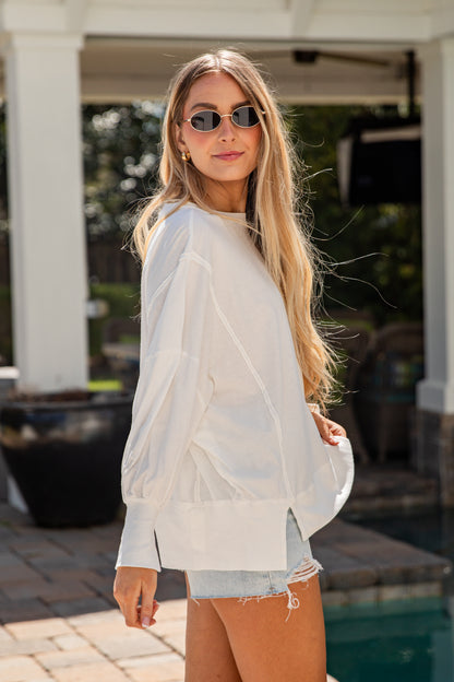 Woman wearing a white sheer top over a denim shirt with sunglasses outdoors.