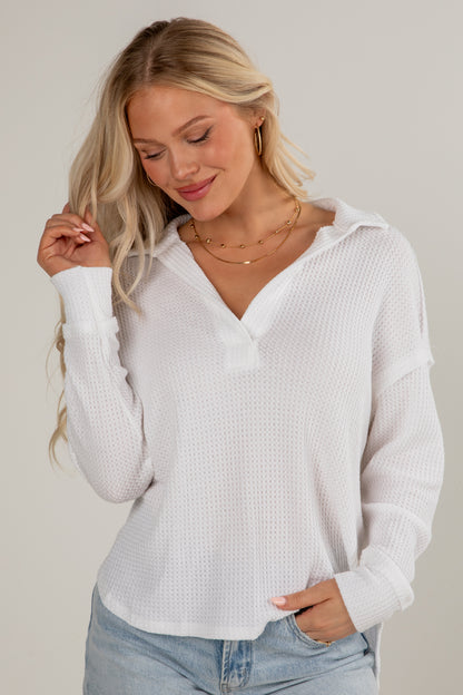 Woman wearing a white long-sleeve top and light blue jeans against a plain background