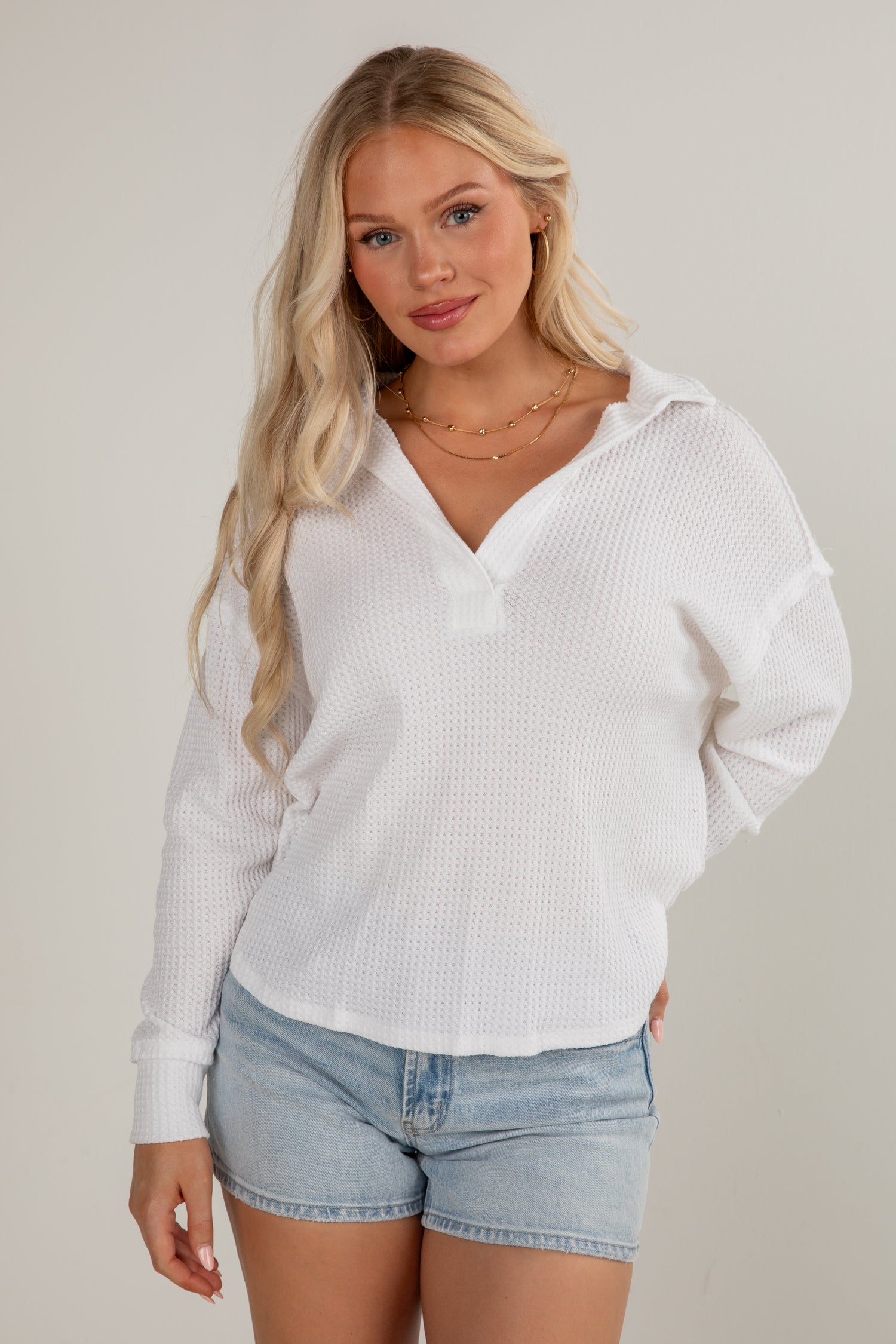 Woman wearing a white ribbed sweater and denim shorts on a plain background