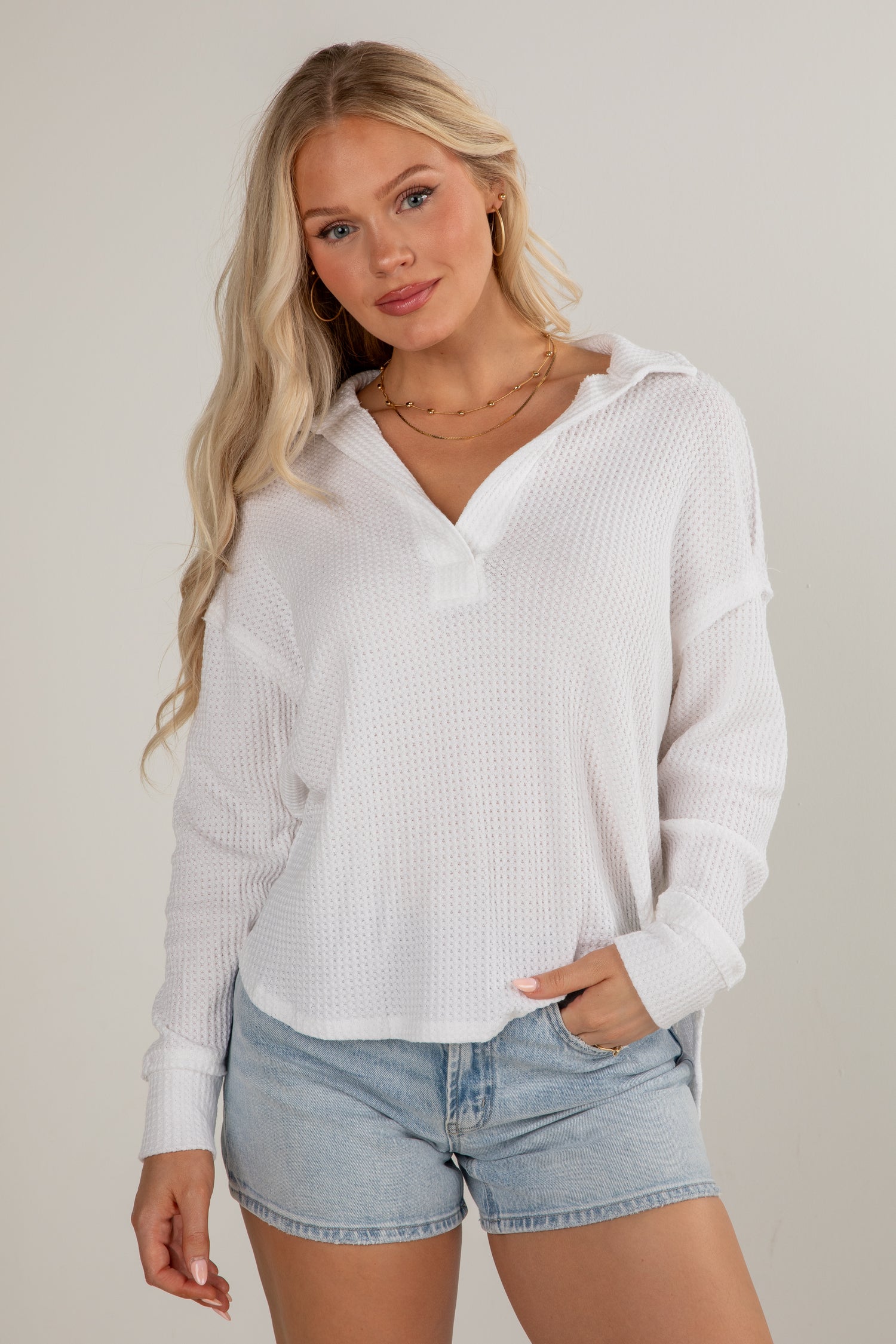 Woman wearing a white ribbed hoodie and denim shorts on a plain background