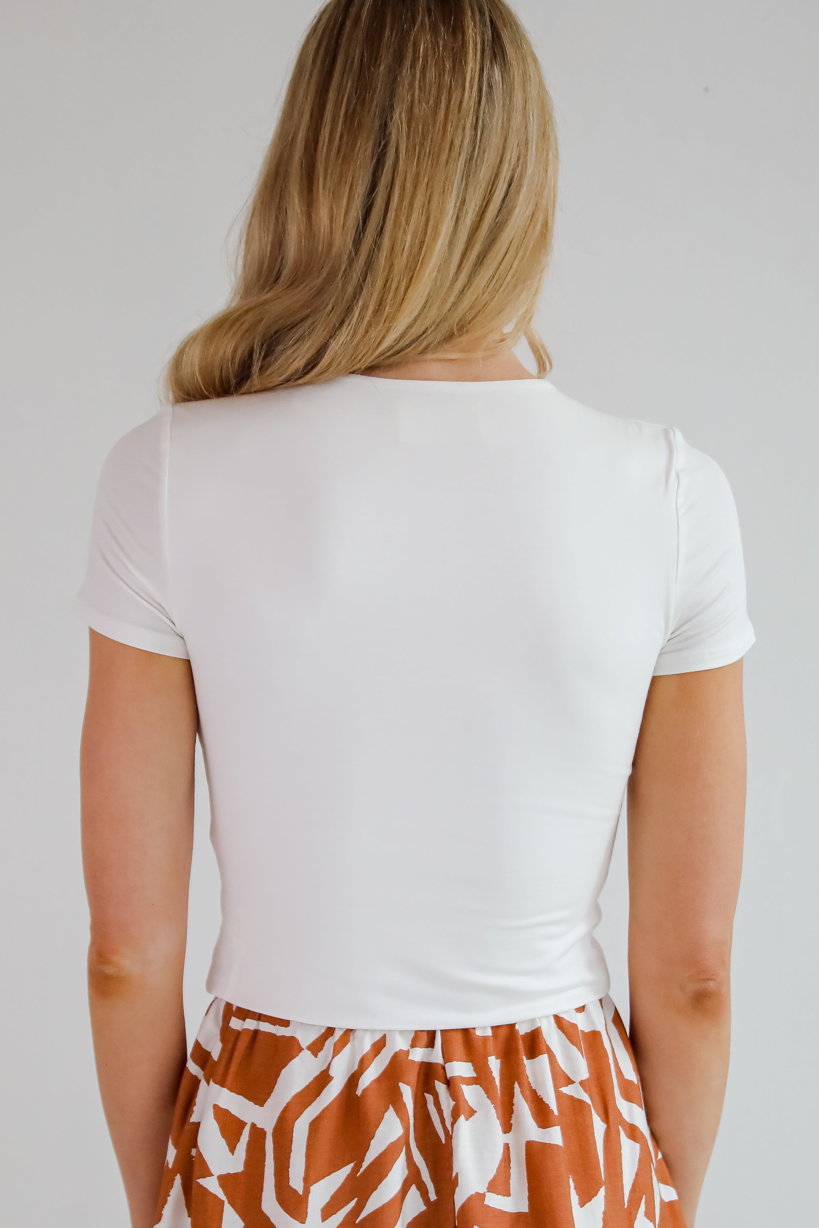 Person wearing a white t-shirt and patterned shorts on a plain background