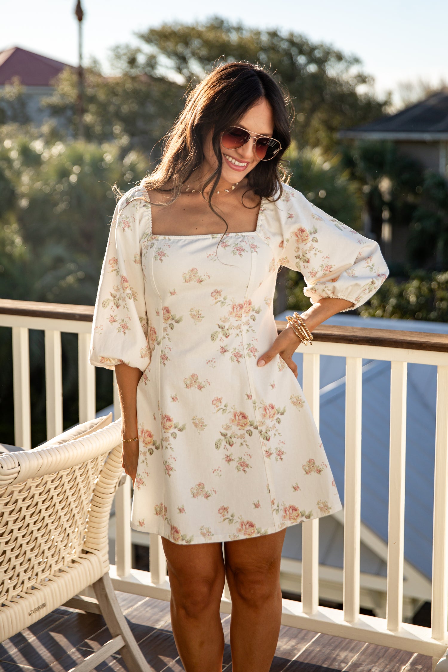 Woman in a floral dress standing on a balcony with trees in the background