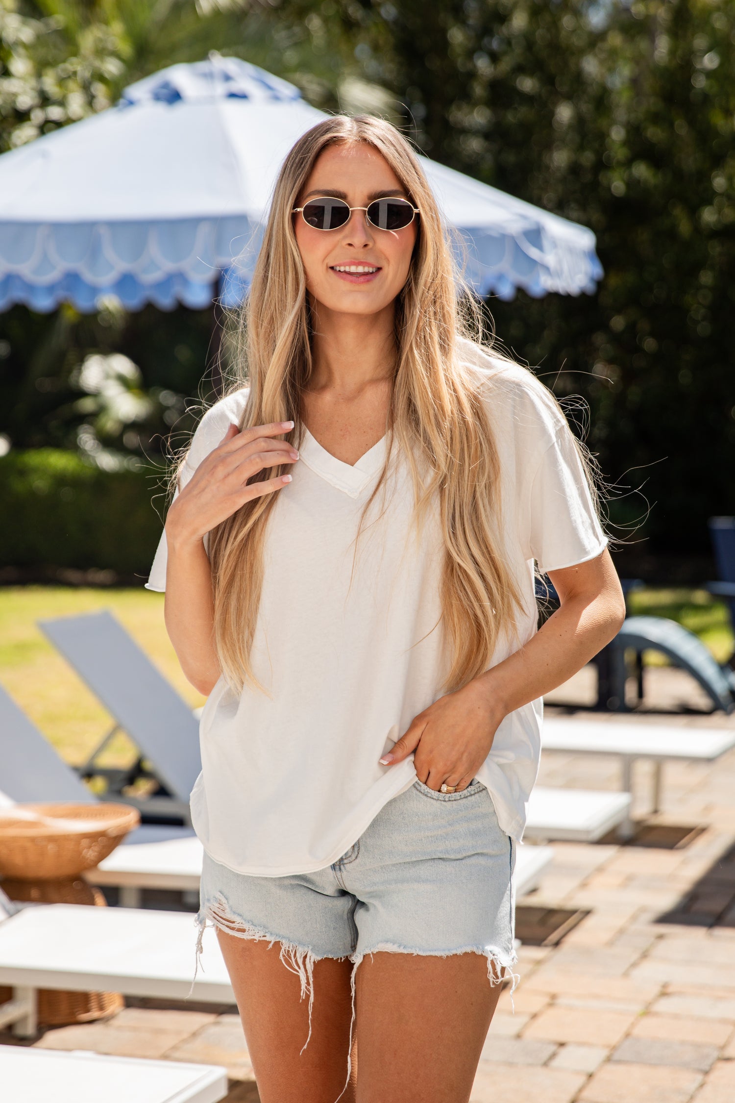 Woman in a white shirt and denim shorts standing outdoors with a blue umbrella in the background.