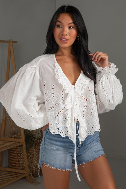 Woman wearing a white lace top and denim shorts in a neutral setting