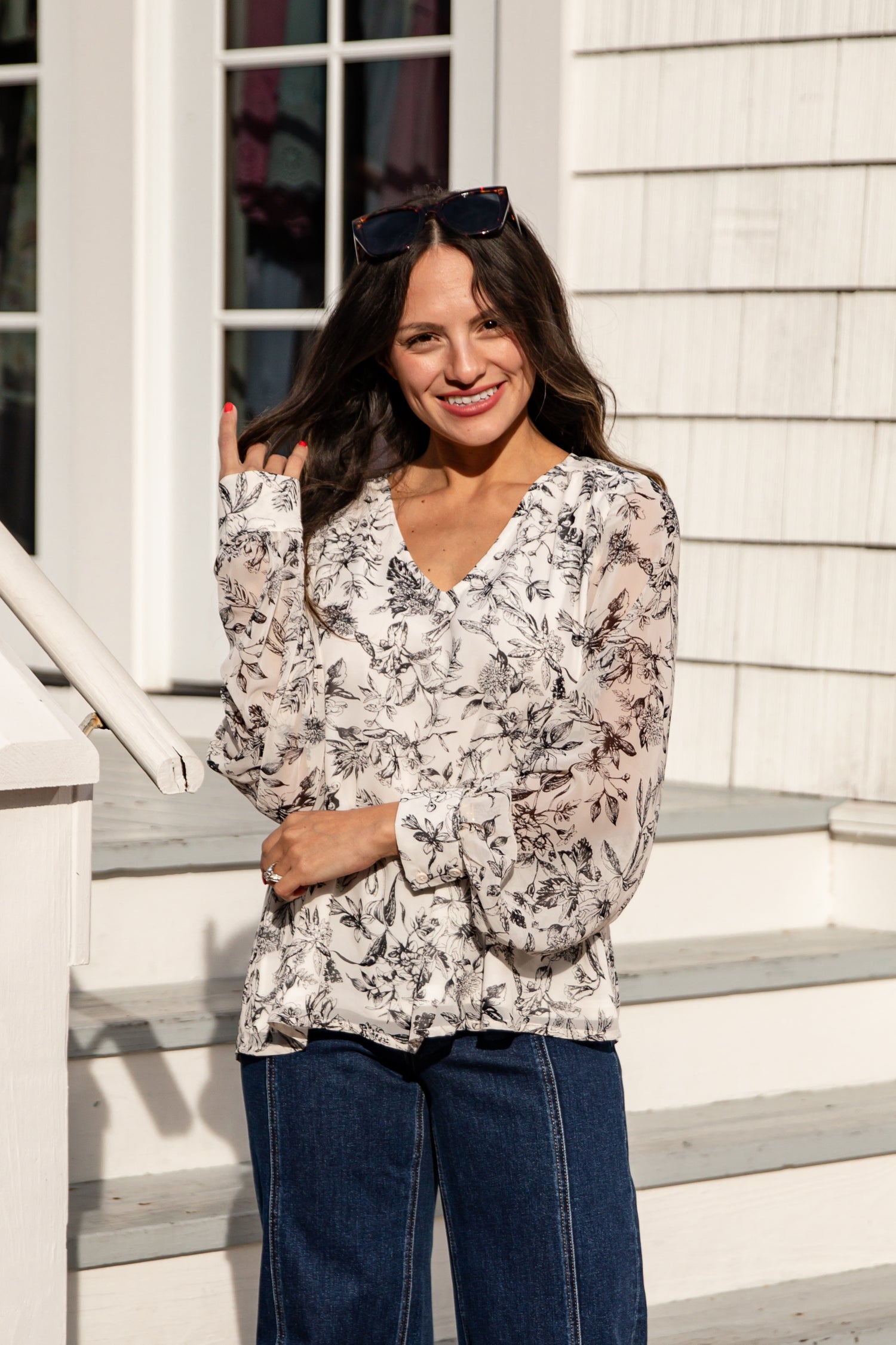 Woman wearing a floral blouse and blue jeans standing on steps outside a house.