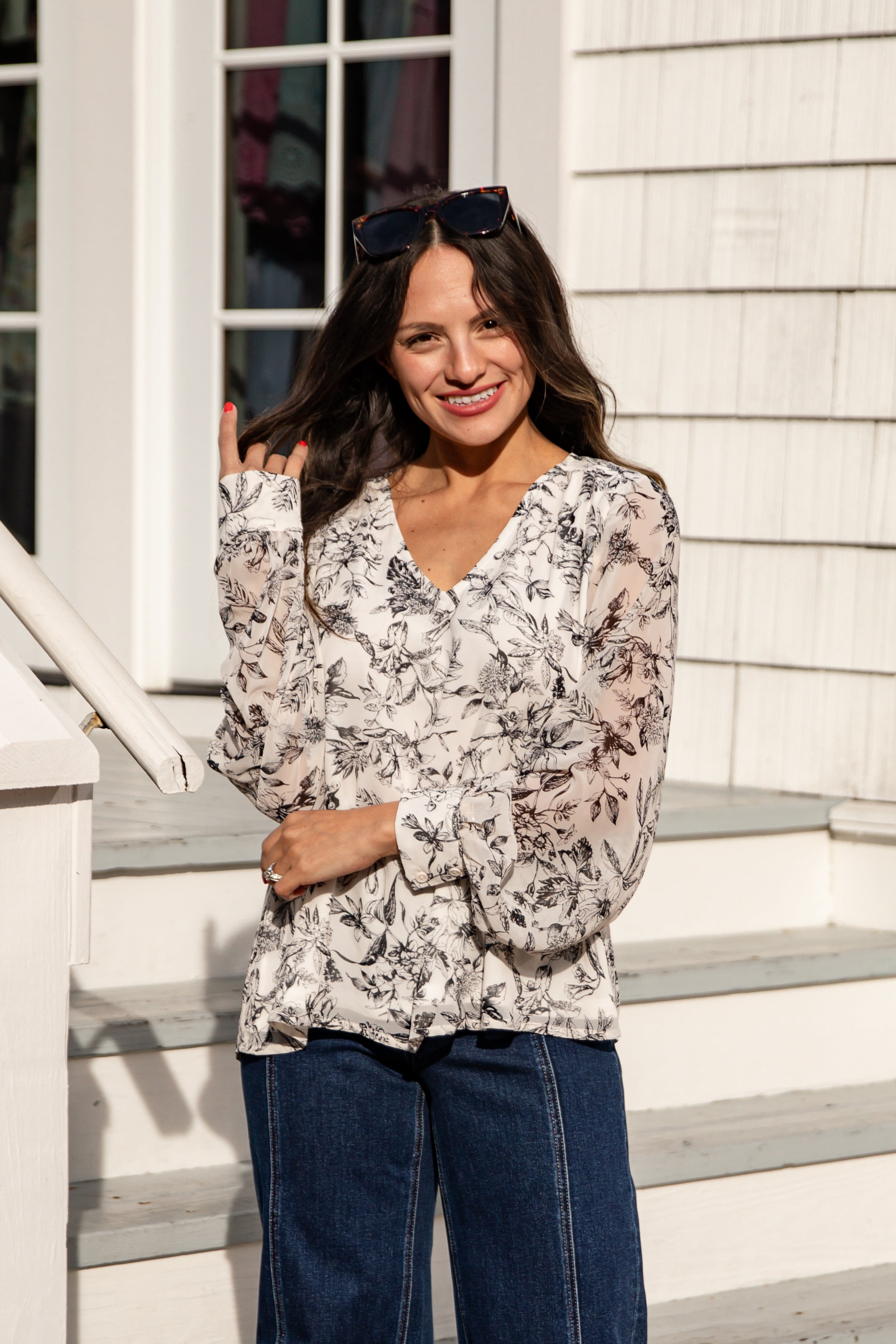 Woman wearing a floral blouse and blue jeans standing on steps outside a house.