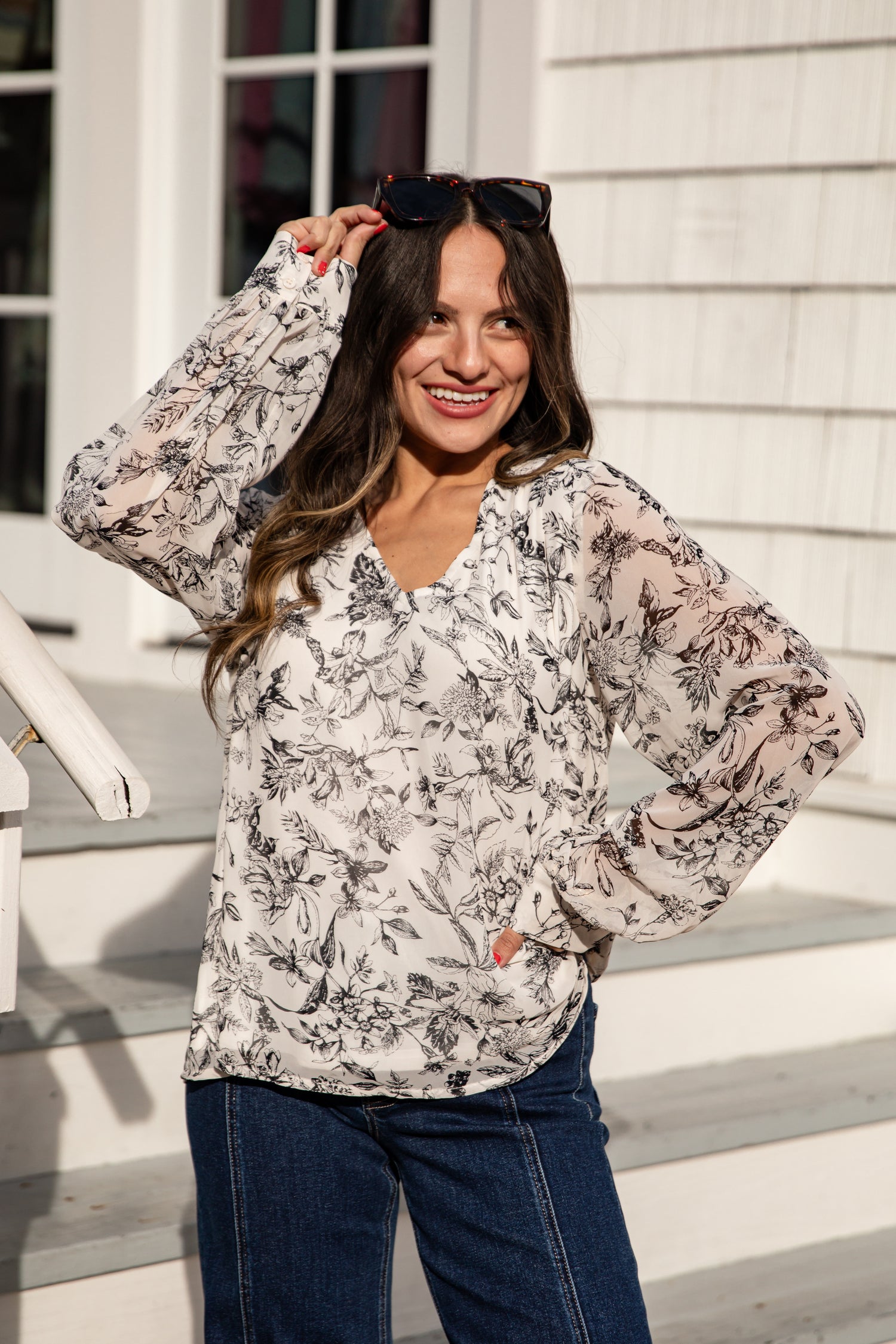 Woman wearing a floral blouse and blue jeans standing on steps.