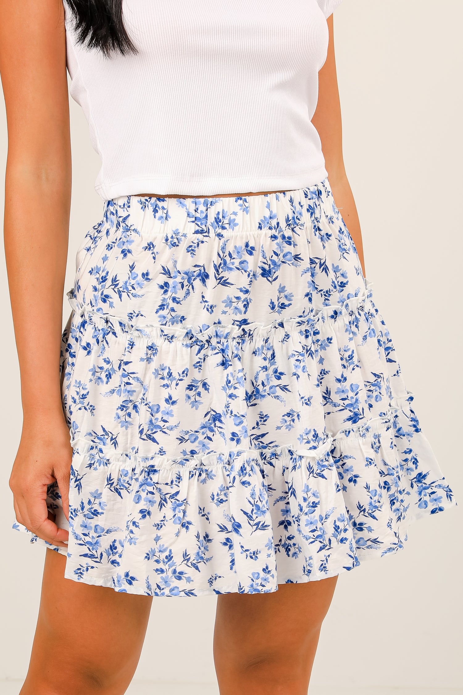 Woman wearing a white floral skirt with blue flowers on a plain background