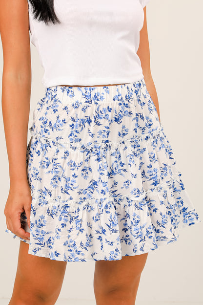 Woman wearing a white floral skirt with blue flowers on a plain background
