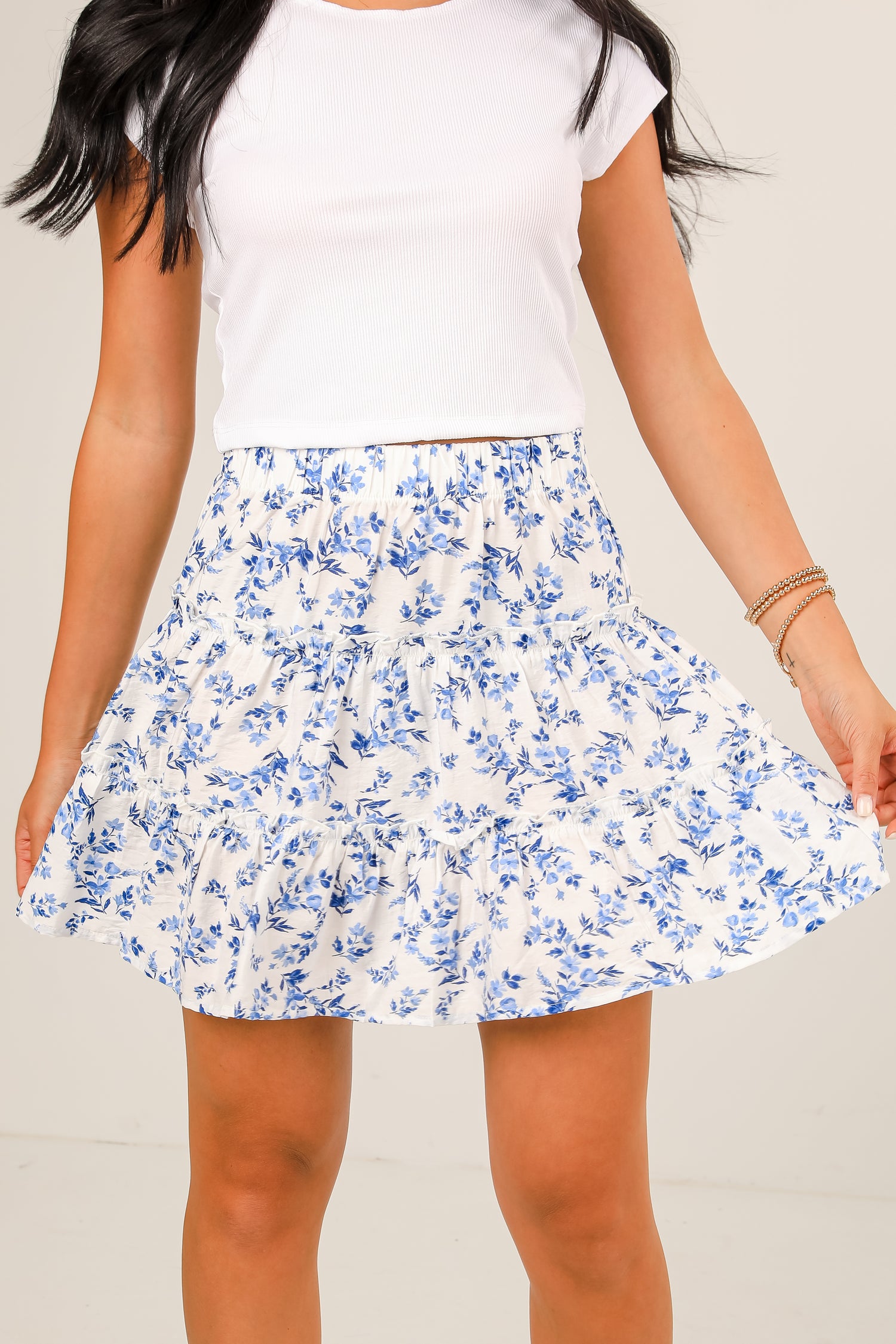 Person wearing a white t-shirt and blue floral skirt on a plain background