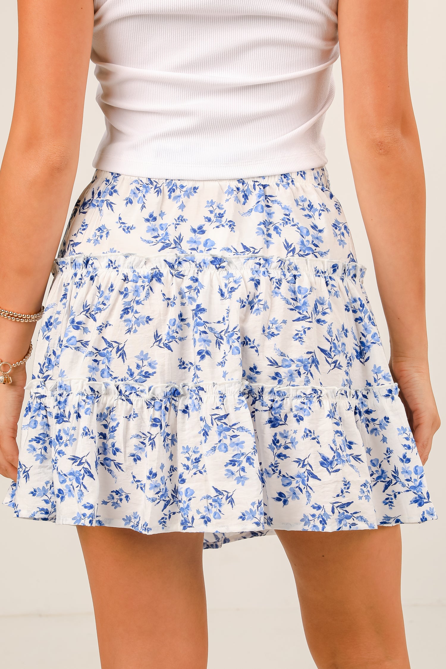 Person wearing a white top and blue floral skirt on a plain background