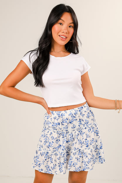 Woman wearing a white crop top and blue floral skirt on a plain background